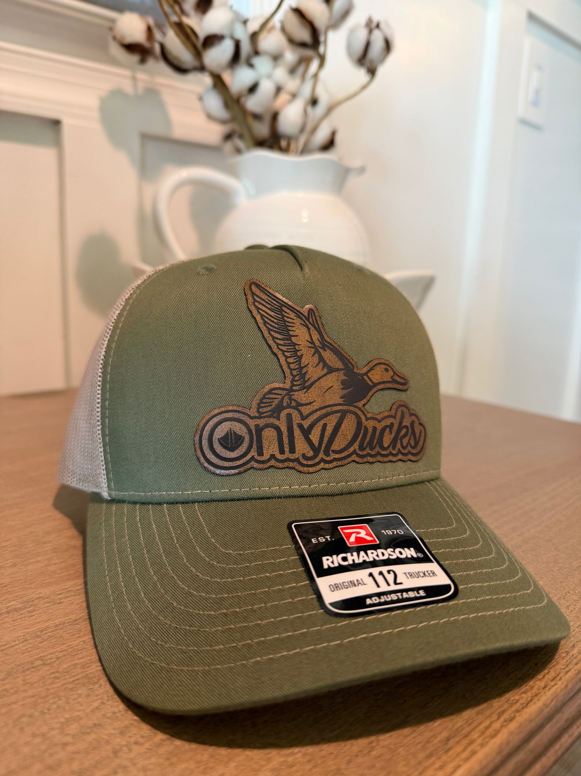 Green and gray cap with 'Only Ducks' logo on a wooden surface